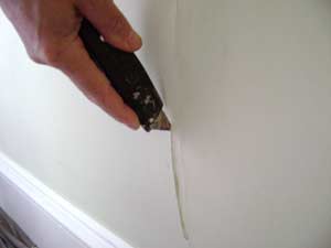 photo cutting out bubbling drywall tape over a wall crack